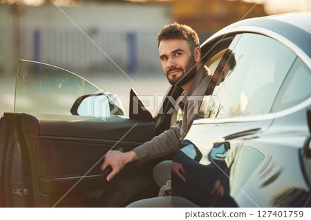 Sitting on the seat. Man is standing near his electric car outdoors 127401759