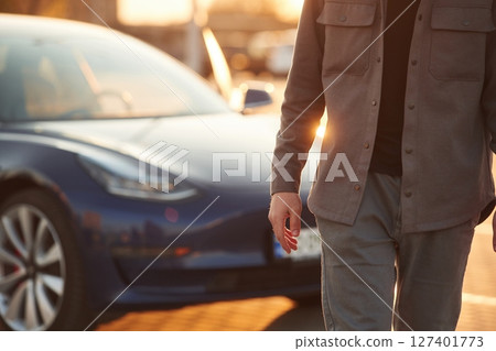 Bright sunlight. Man is standing near his electric car outdoors 127401773