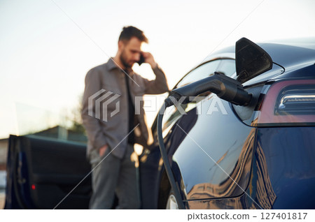In formal clothes. Man is standing near his electric car outdoors 127401817