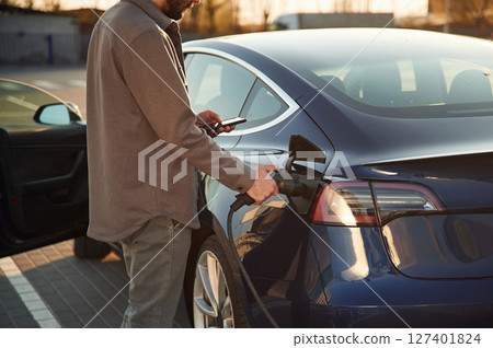 In formal clothes. Man is standing near his electric car outdoors 127401824