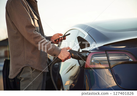 Grey colored formal clothes. Man is standing near his electric car outdoors 127401826