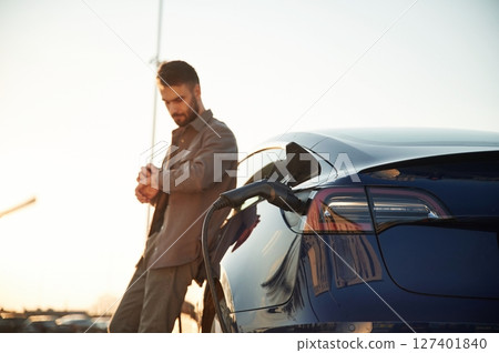 Charging process. Man is standing near his electric car outdoors 127401840