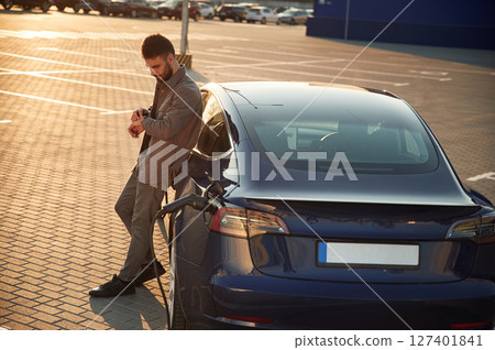 On the charging station. Man is standing near his electric car outdoors 127401841
