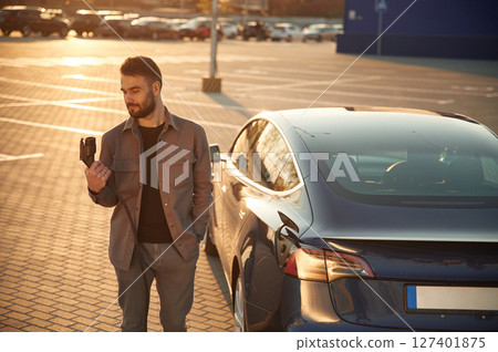 Waiting for the automobile to charge. Man is standing near his electric car outdoors Waiting for the automobile to charge. Man is standing near his electric car outdoors 127401875