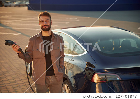 Time to charge the automobile. Man is standing near his electric car outdoors Time to charge the automobile. Man is standing near his electric car outdoors 127401878