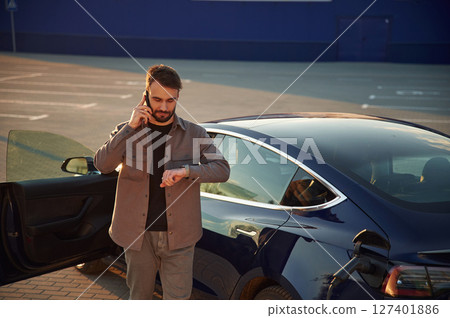Business call by phone. Man is standing near his electric car outdoors 127401886