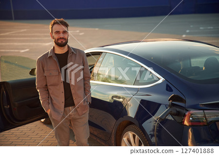 Gorgeous stylish man is standing near his electric car outdoors 127401888