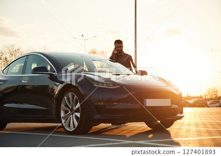 Beautiful sunlight. Man is standing near his electric car outdoors Beautiful sunlight. Man is standing near his electric car outdoors 127401893
