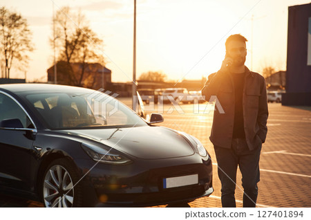 Beautiful sunlight. Man is standing near his electric car outdoors 127401894