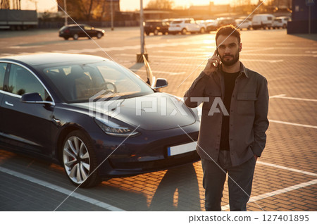 Evening time. Beautiful sunlight. Man is standing near his electric car outdoors 127401895