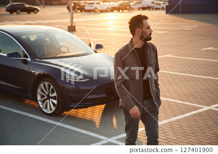 Handsome man is standing near his electric car outdoors Handsome man is standing near his electric car outdoors 127401900