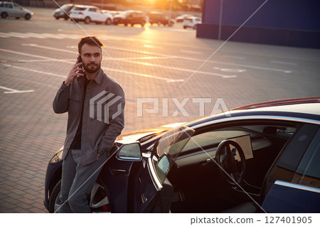 Evening time. Beautiful sunlight. Man is standing near his electric car outdoors 127401905