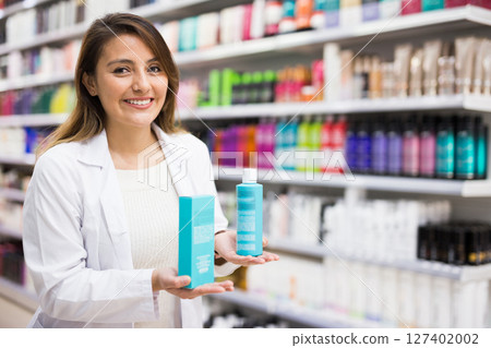 Positive salesgirl helping to choose hair products in cosmetic store 127402002