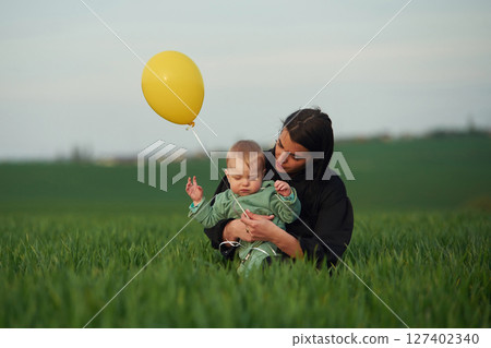 Mother with her little baby son is outdoors on the agricultural field. With yellow balloon Mother with her little baby son is outdoors on the agricultural field. With yellow balloon 127402340