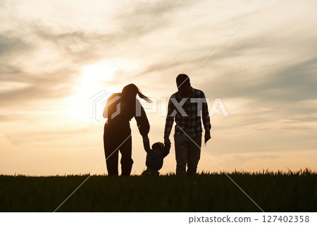 Silhouettes of father, mother and little baby son is outdoors against sunset dramatic sky in the field 127402358