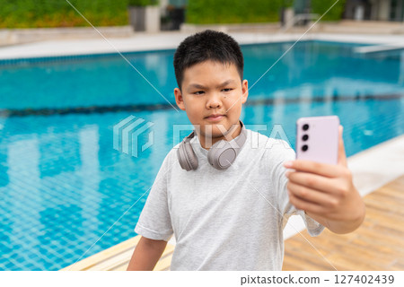 Teenage Boy at Poolside During Summer Using Phone 127402439