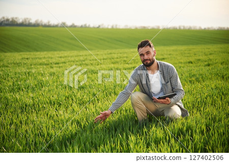 Sitting, holding notepad and checking quality of wheat. Handsome young man is on agricultural field 127402506