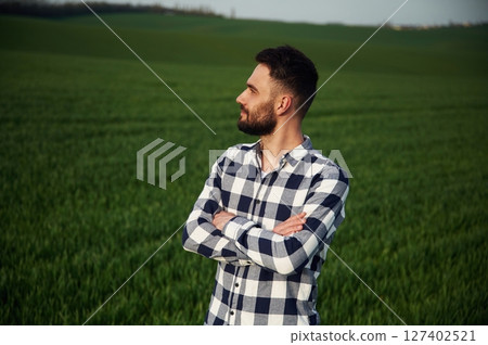 Standing with arms crossed. Handsome young man is on agricultural field 127402521