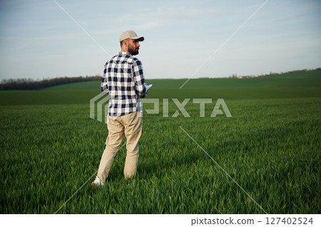 Walking, holding notepad. Handsome young man is on agricultural field 127402524