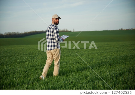 Walking, holding notepad. Handsome young man is on agricultural field 127402525