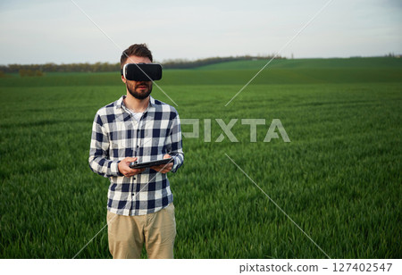 In virtual reality glasses. Handsome young man is on agricultural field 127402547