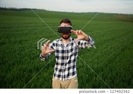 Black virtual reality glasses. Playing game. Handsome young man is on agricultural field 127402562