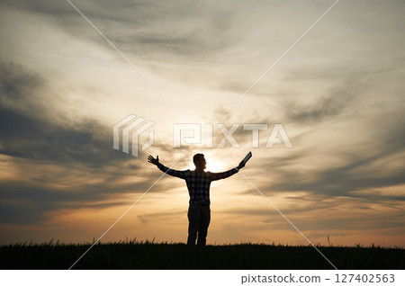 Silhouette of a man that is in the field at sunset time. Dramatic sky 127402563