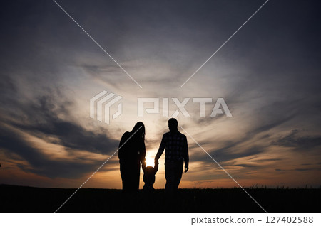 Silhouettes of father, mother and little baby son is outdoors against sunset dramatic sky in the field 127402588