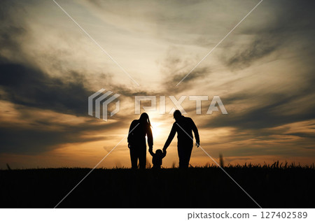 Silhouettes of father, mother and little baby son is outdoors against sunset dramatic sky in the field 127402589