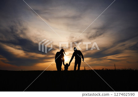 Silhouettes of father, mother and little baby son is outdoors against sunset dramatic sky in the field 127402590