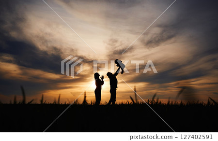 Holding little baby in hands. Silhouettes of father and mother that are outdoors against sunset dramatic sky in the field 127402591