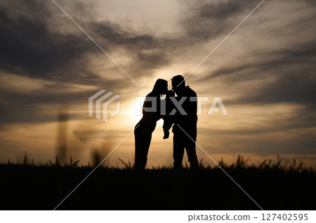 Silhouettes of father, mother and little baby son is outdoors against sunset dramatic sky in the field 127402595