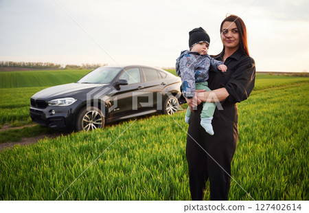Against he modern car. Mother with her little baby son is outdoors on the agricultural field 127402614