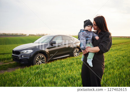 Against he modern car. Mother with her little baby son is outdoors on the agricultural field 127402615