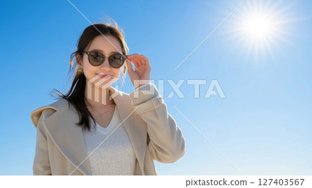 Smiling woman wearing sunglasses against blue sky Smiling woman wearing sunglasses against blue sky 127403567