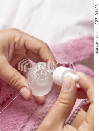 Closeup of young woman in pink bathrobe opening dropper bottle top view, cosmetic mockup Closeup of young woman in pink bathrobe opening dropper bottle top view, cosmetic mockup 127404108