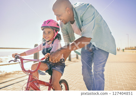 Black girl, bike and learning with dad, smile and park in sunshine, safety or happiness by sea. Father, kid and bicycle for summer training, childhood development and outdoor in street with helmet 127404851