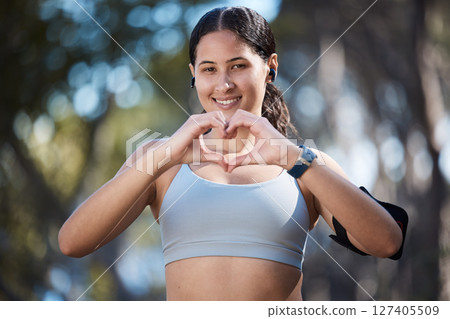 Fitness portrait, heart hands and woman in nature with sign for affection or love emoji outdoors. Health, wellness and female athlete in park with hand symbol for support while preparing for training 127405509
