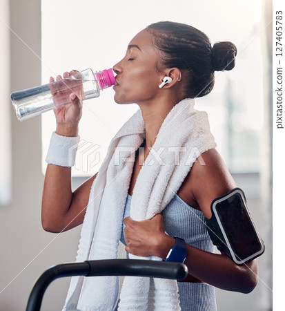 Drinking water, fitness and smartphone on woman arm gym gear, technology and listening to music for workout on stationary cycling machine. Tired, challenge and motivation black woman cardio training 127405783