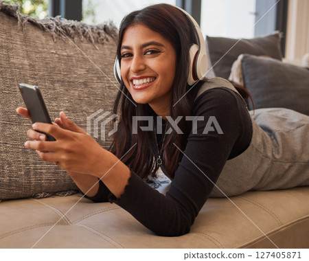 Woman, smile and phone listening to music with headset while relaxing on living room sofa. Portrait of happy female in relax and enjoying audio track, chatting or texting on smartphone on the couch Woman, smile and phone listening to music with headset while relaxing on living room sofa. Portrait of happy female in relax and enjoying audio track, chatting or texting on smartphone on the couch 127405871