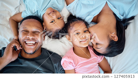 Happy family, love and relax in bed together for support, care and quality time bonding. Parents, children and mom kiss girl face for affection, happiness and beautiful portrait in family home 127405913