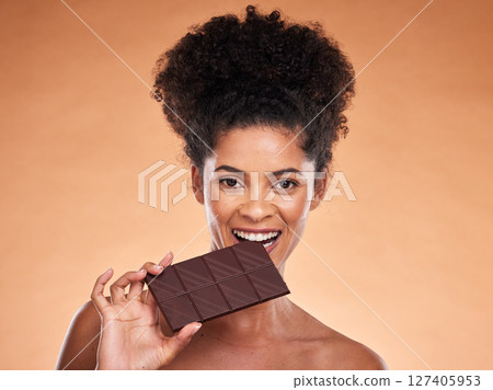 Chocolate, happy woman and beauty portrait, studio background and eating sweets, cacao dessert and enjoy sugar. Black woman bite chocolate bar, cocoa and candy, diet calories and snack temptation 127405953