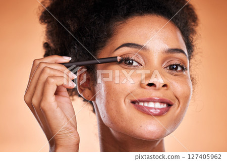 Beauty, skincare and makeup with black woman using eyeliner on eye for facial cosmetics product on a orange studio background. Face portrait of aesthetic model with smile and happiness for self care 127405962