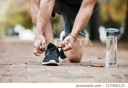 Fitness, exercise and running shoes while tying shoelace on ground with water bottle for cardio workout or training. Hands of man with sneakers outdoor for run and performance for health and wellness 127406125