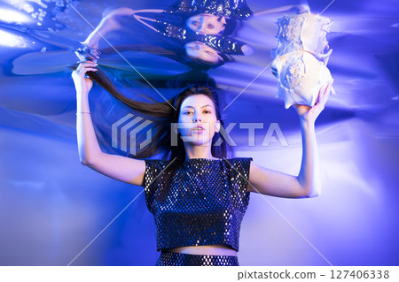 Girl Dressed as a Mermaid Glimmers Underwater While Holding a Seashell in Vibrant Blue Lighting 127406338