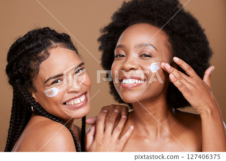 Beauty, friends and black women with face cream for skincare or moisturizing in studio on brown background. Smile, group portrait and models apply facial product or cosmetics creme for healthy skin. Beauty, friends and black women with face cream for skincare or moisturizing in studio on brown background. Smile, group portrait and models apply facial product or cosmetics creme for healthy skin. 127406375