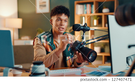 Influencer, camera and man with mic for podcast, review or social media broadcast. Filming, product or content creator show tech for photography, ratings or picture quality for live streaming at home Influencer, camera and man with mic for podcast, review or social media broadcast. Filming, product or content creator show tech for photography, ratings or picture quality for live streaming at home 127407471