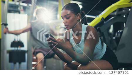 Fitness, smartphone or woman in gym, internet and online reading with social media, chat or workout. Resting, mobile user or healthy person in wellness center, cellphone or app for exercise goal 127407501