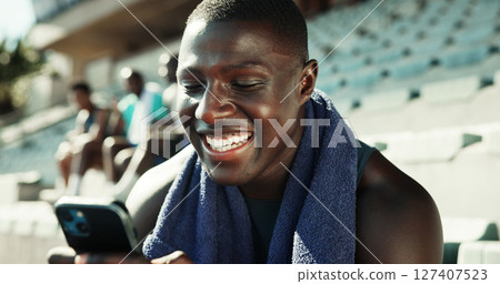 Athlete, man and happy with phone on stadium for workout post, streaming service or social media scroll. Fitness, runner and smartphone at sports arena for practice break, text message or mobile chat 127407523