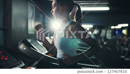 Fitness, woman and running on treadmill in gym at night for agility training, speed development or calorie burning. Flare, evening workout or girl on machine for cardio exercise or muscle performance 127407610